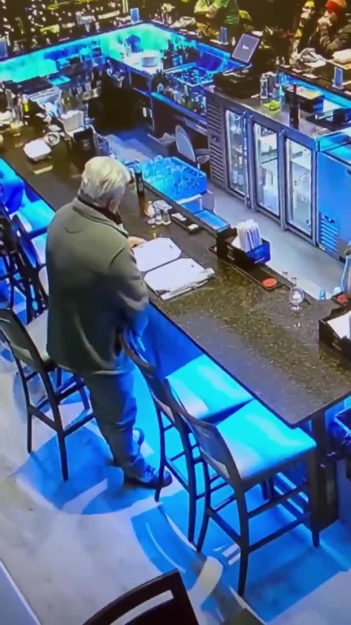 A man pretending to look at a menu at the bar while he takes a piss next to it