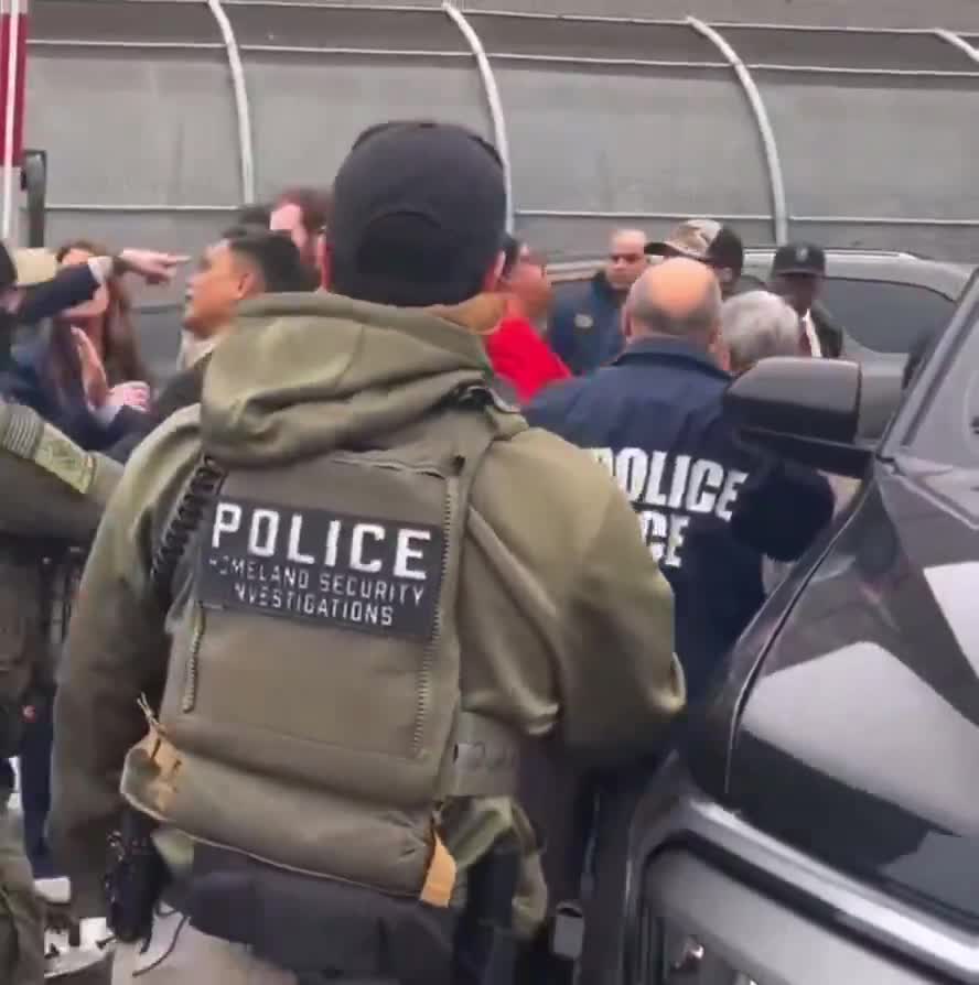 Rep. LaMonica McIver (red jacket) shouts in the faces of ICE officers